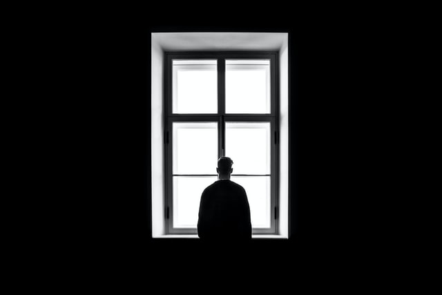 παρανοειδής διαταραχή προσωπικότητας άνδρας σε σκοτεινό δωμάτιο κοιτάει από το παράθυρο